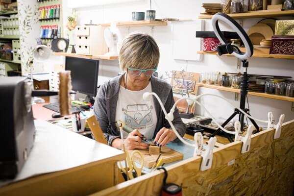 Conchita está sentada y tallando una madera sobre la mesa del taller de Samu-Do.